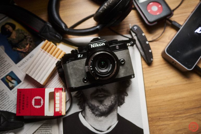 Nikon Zf camera, cigarettes, headphones, phone, and a knife on a wooden surface.