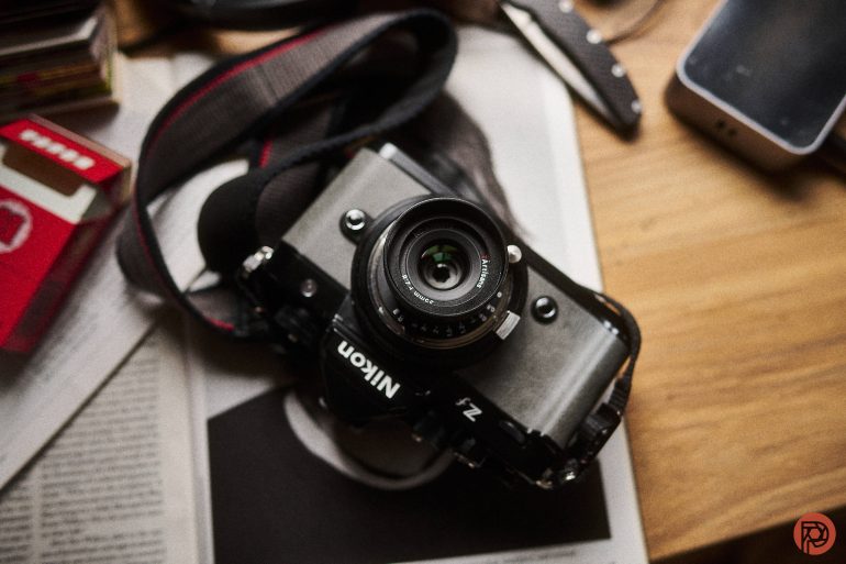 A Nikon Z fc camera with a 7Artisans 35mm f/2.8 lens is resting on a newspaper.