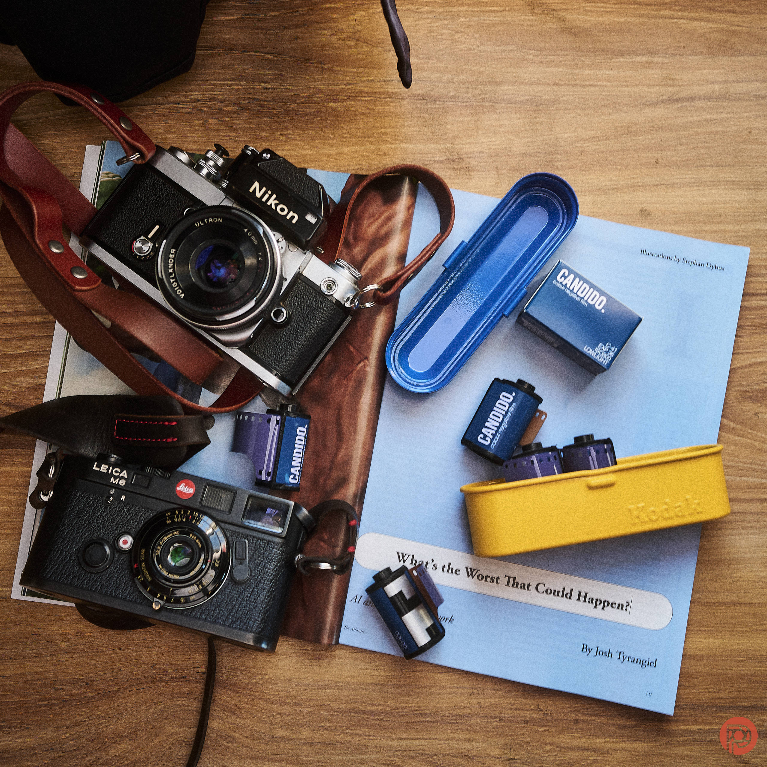 Did You Get Scammed? A Photographer's Guide to Buying Used Cameras Two vintage cameras, film rolls, and film cases on an open magazine atop a wooden surface.