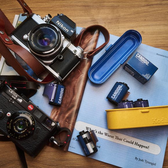 Two vintage cameras, film rolls, and film boxes on a wooden table with a magazine and cases.
