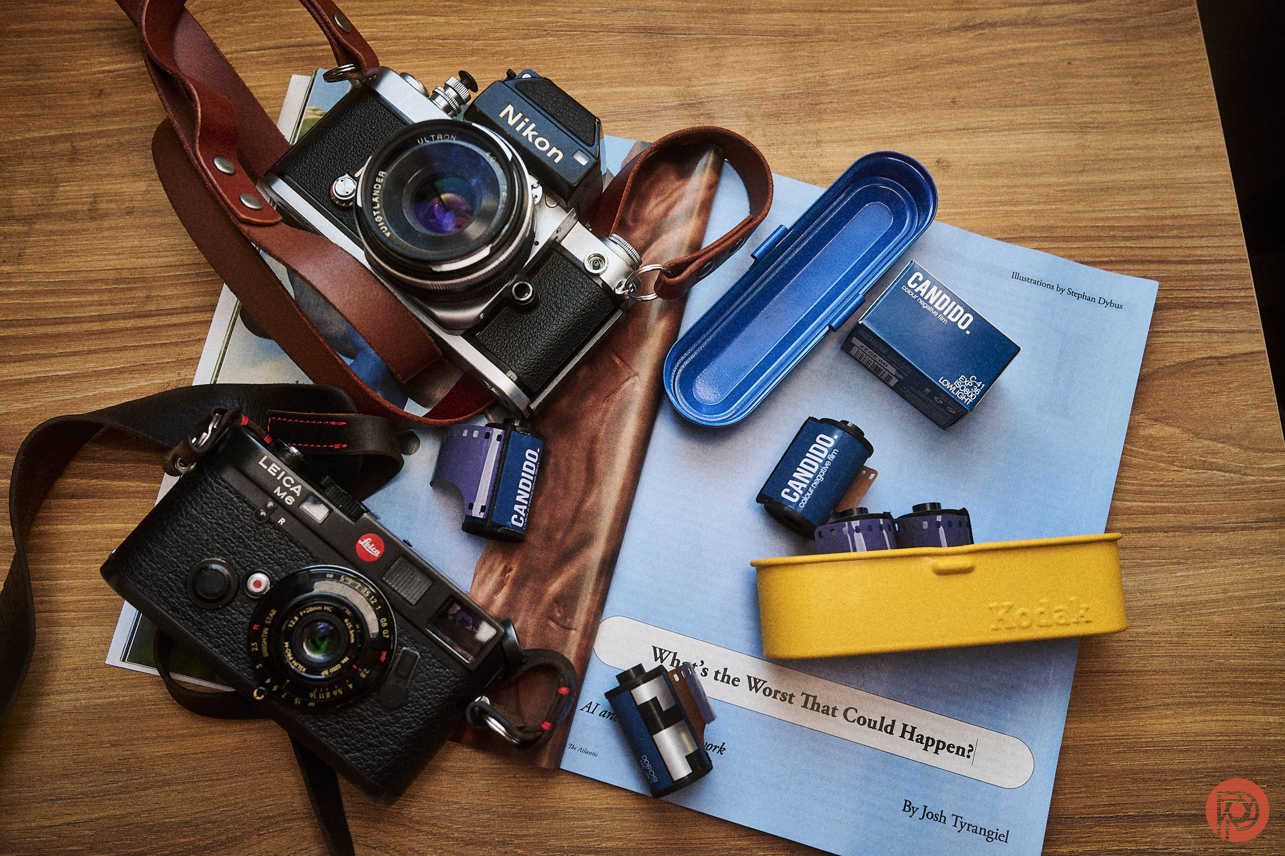 Two vintage cameras, film rolls, and film boxes on a wooden table with a magazine and cases.