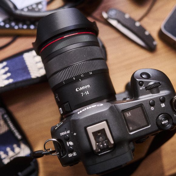 A Canon camera with a 7-14mm lens and strap is shown on a wooden surface.