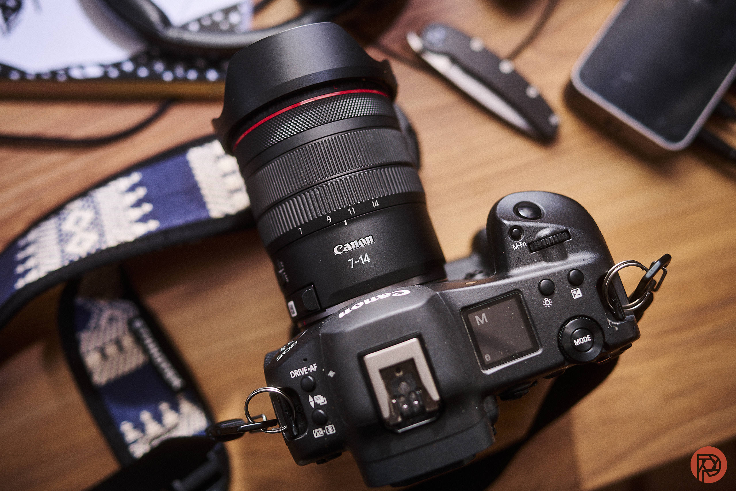Canon RF 7-14mm f2.8-3.5 L Review: A Canon camera with a 7-14mm lens and strap is shown on a wooden surface.