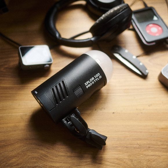 A portable strobe light sits on a wooden table next to headphones and a media player.