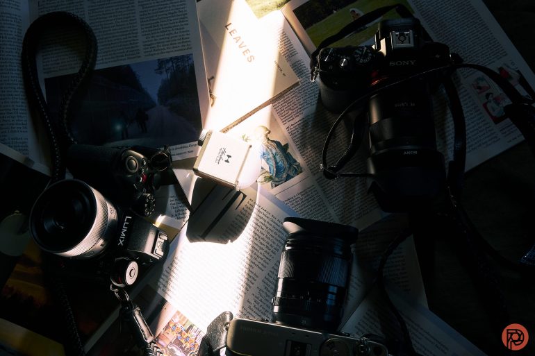 Three cameras and a lens rest on open magazines, lit by a beam of sunlight from above.