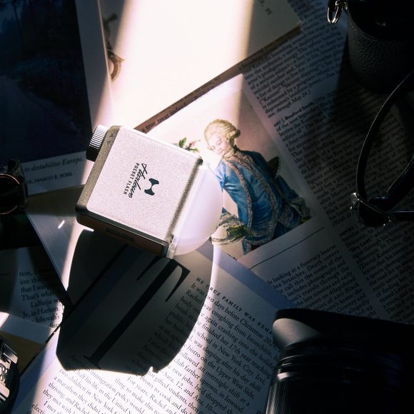 Flat lay of camera gear, magazines, and a card reader under dramatic light with shadows across the scene.