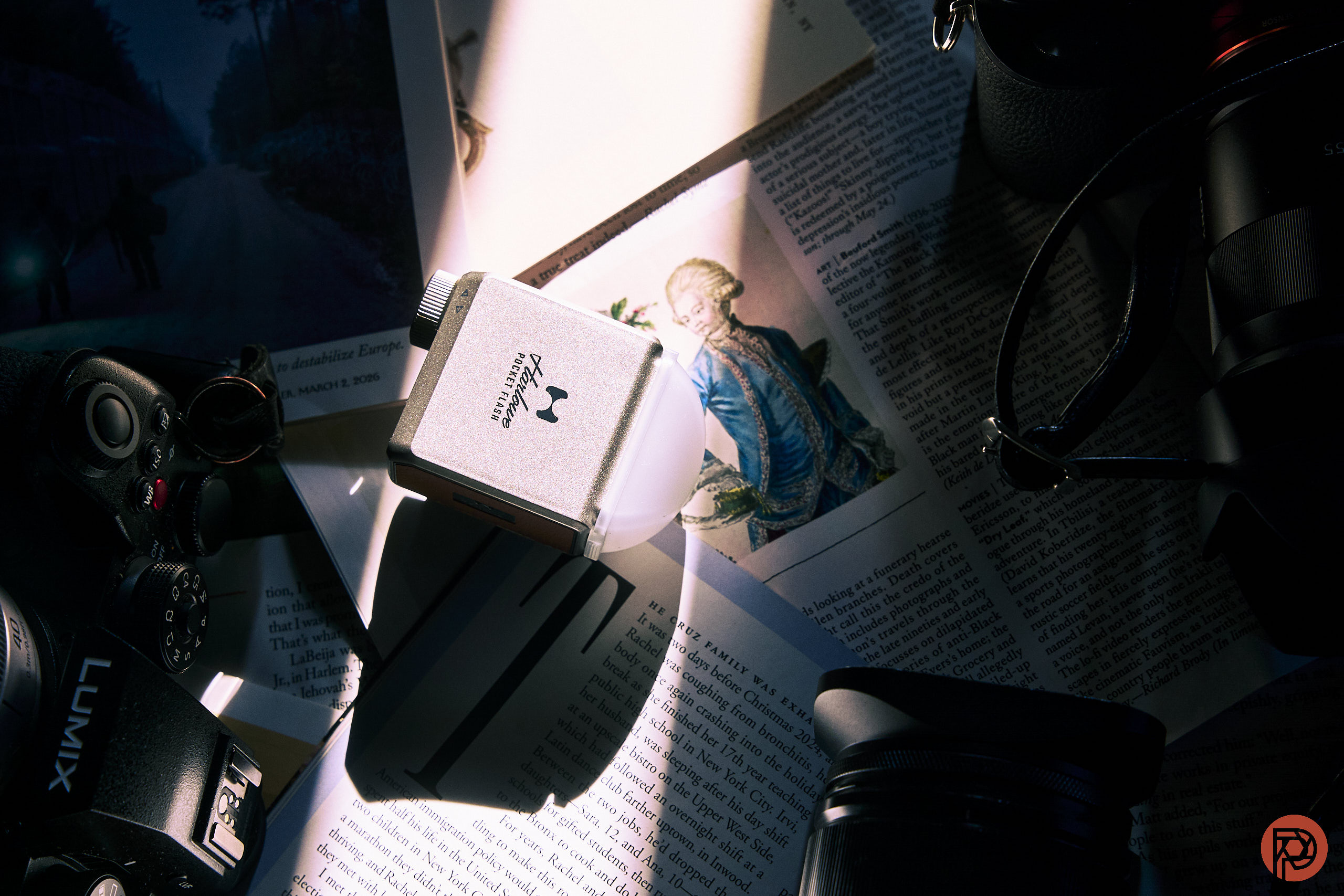 Flat lay of camera gear, magazines, and a card reader under dramatic light with shadows across the scene.