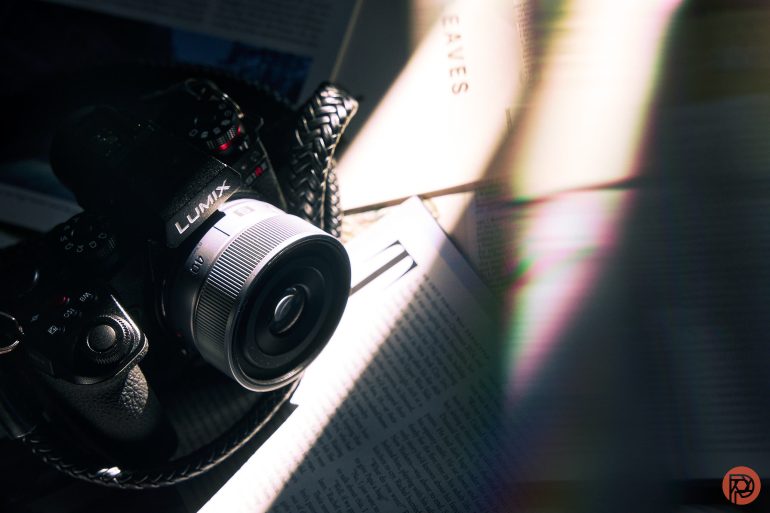 A Lumix camera on open books, with sunlight and rainbow light streaks across the pages.