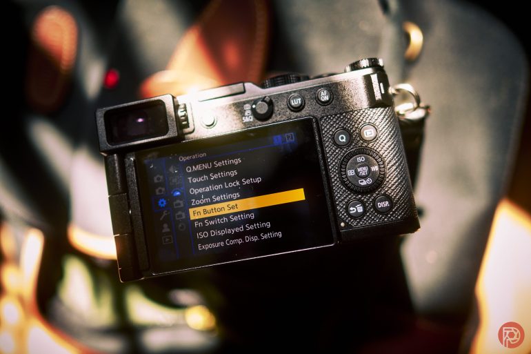 A digital camera displays its settings menu with Zoom Settings highlighted on the screen.