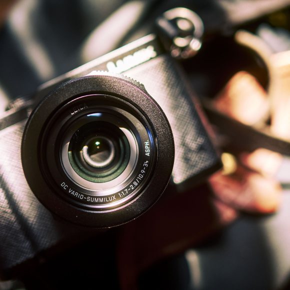 Close-up of a black camera with a large lens, angled and illuminated by bright natural sunlight.