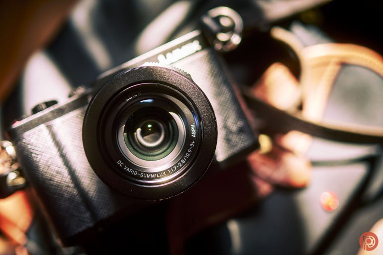 Close-up of a black camera with a large lens, angled and illuminated by bright natural sunlight.