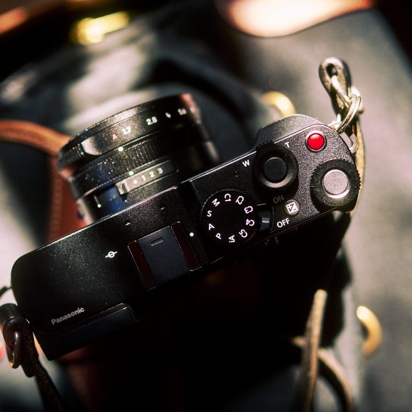 A black Panasonic camera rests on a bag, sunlight highlighting its buttons and dials.