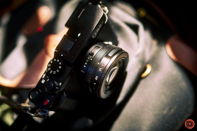 A black Panasonic Lumix camera rests on a dark fabric surface with brown leather accents.
