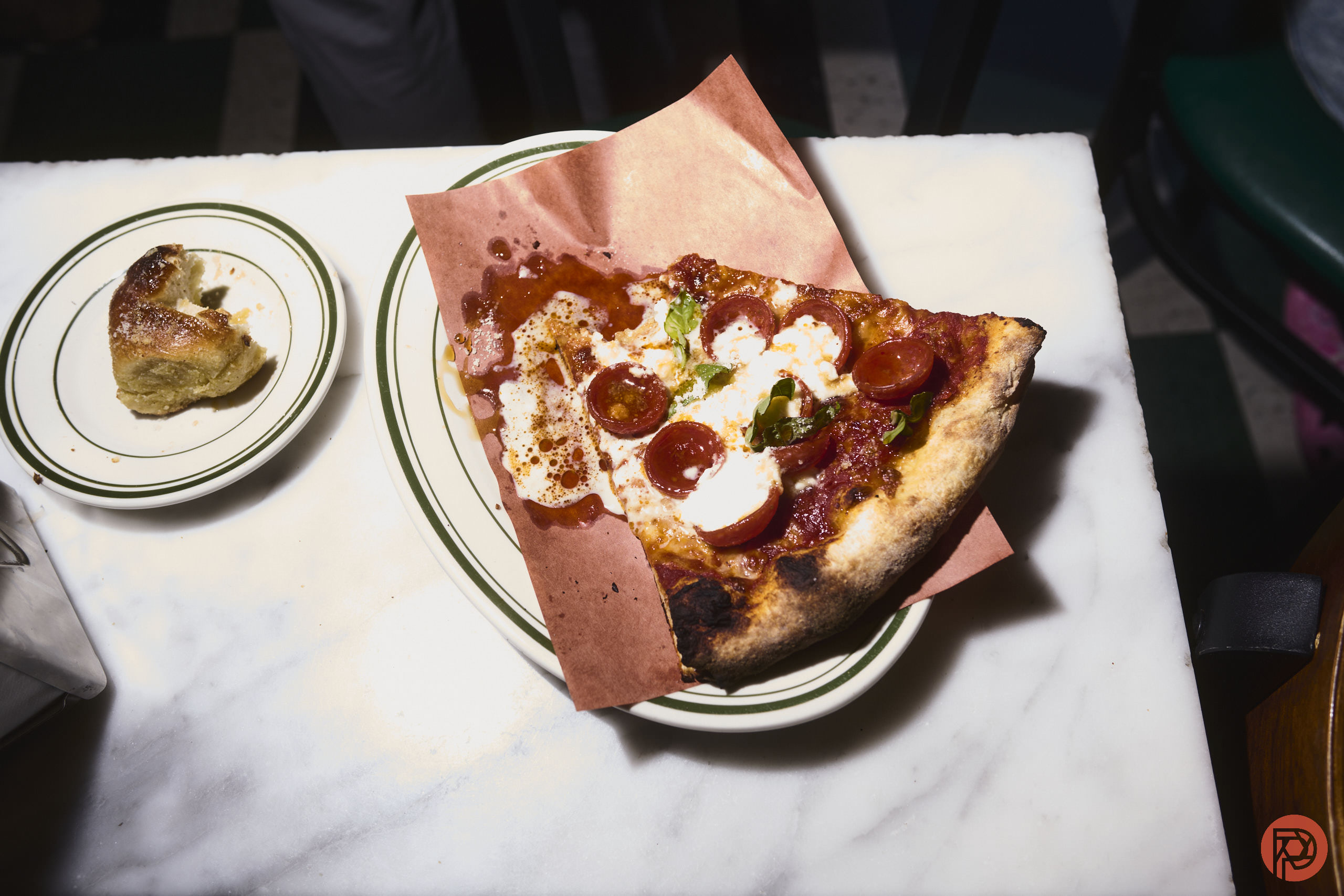 A slice of pepperoni pizza on a plate with a small pastry on a side dish on a marble table.