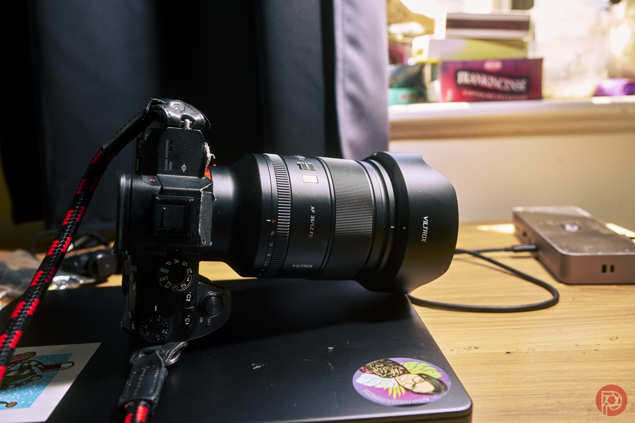 A camera with a large lens rests on a closed laptop on a wooden desk near a window.