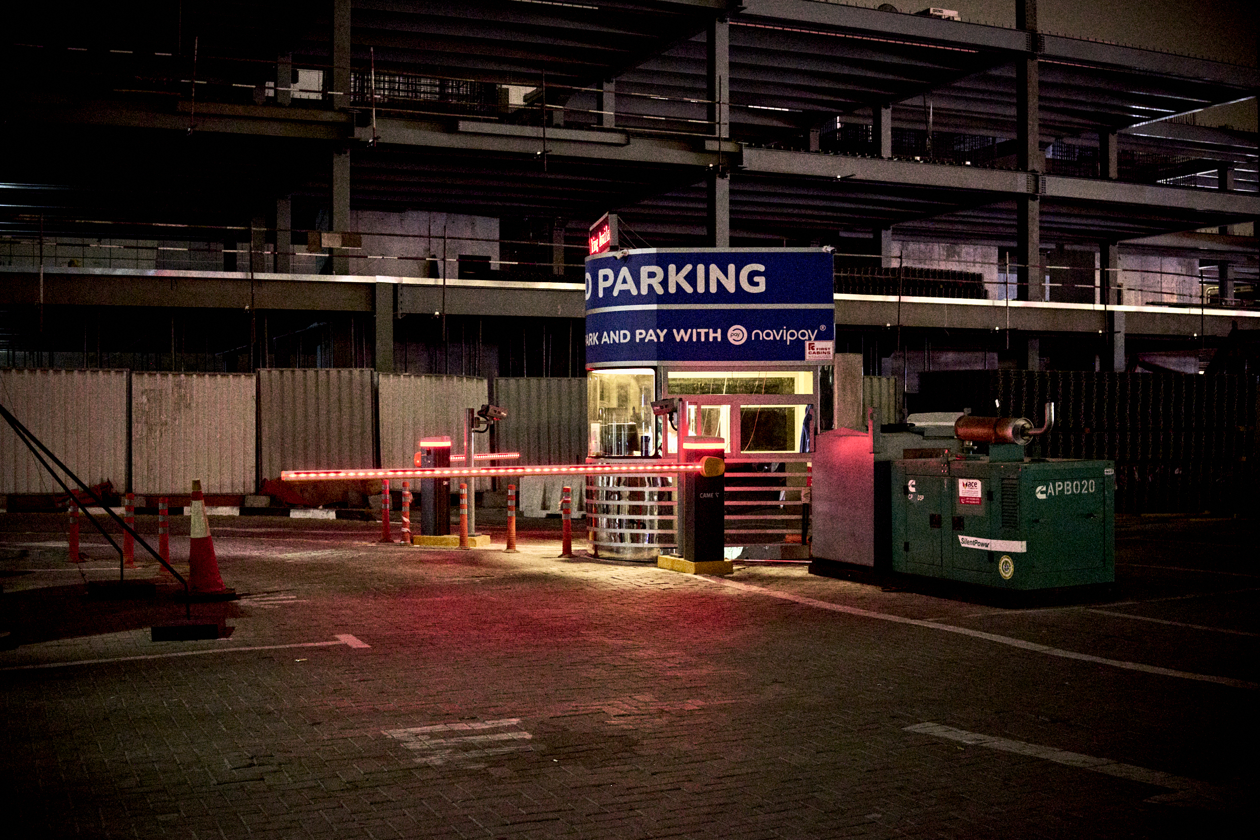 A parking lot entrance at night with a lit barrier gate and a small payment booth.