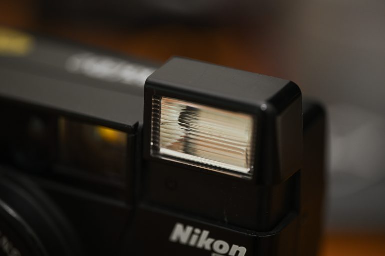 Close-up of a Nikon cameras flash unit, with the lens and logo partially visible in the frame.