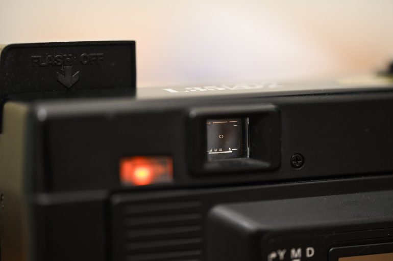 Close-up view of a black camera’s viewfinder with a red indicator light and FLASH OFF label visible.