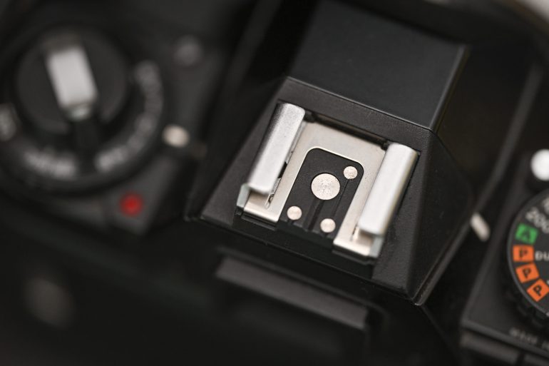 Close-up of a camera hot shoe mount with dials and controls visible around it.