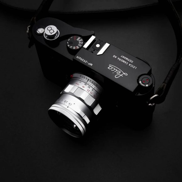 A black Leica camera with a silver lens resting on a dark surface, seen from above.