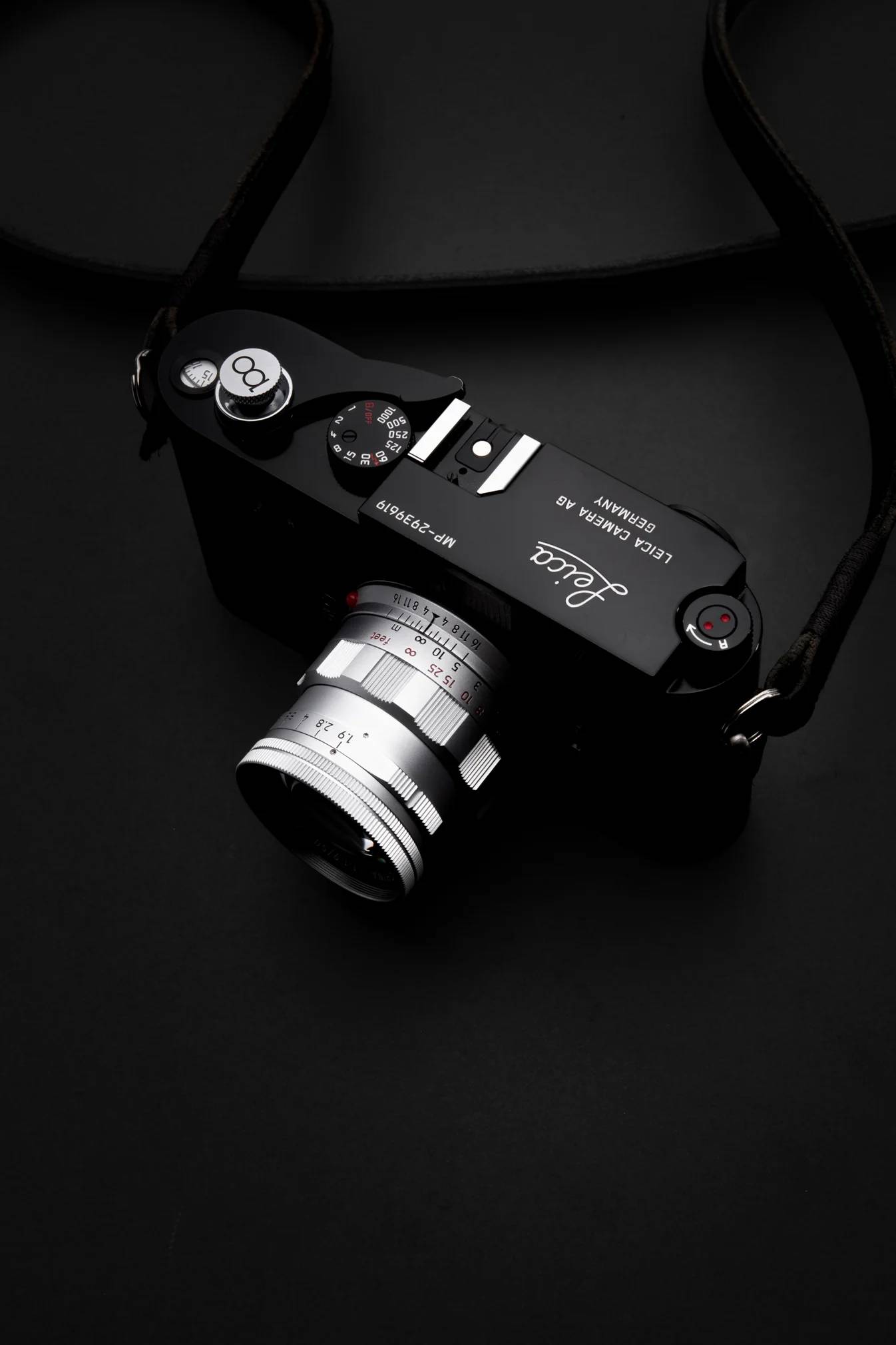A black Leica camera with a silver lens resting on a dark surface, seen from above.