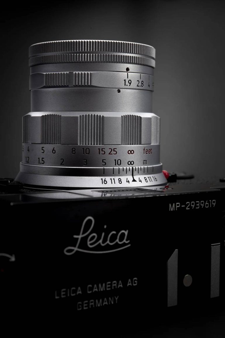 Close-up of a silver Leica camera lens with focus and aperture markings, mounted on a Leica camera body.