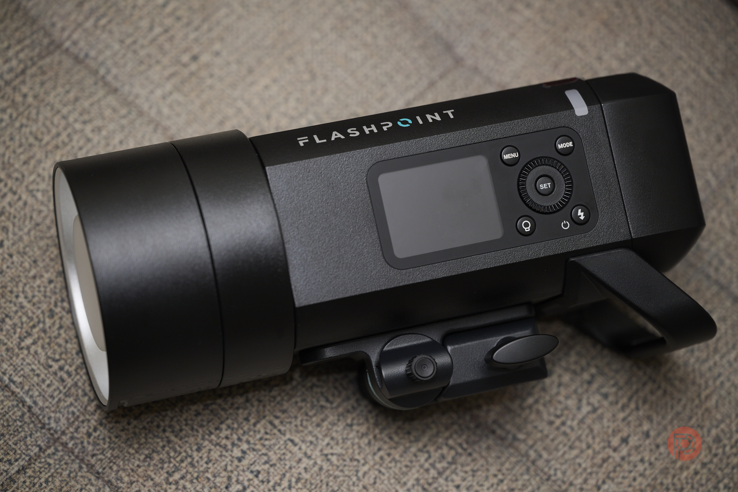 Flashpoint XPLOR 400 Pro II Strobe - An Unmissable Upgrade Black Flashpoint camera flash unit with control buttons and display, placed on a textured beige surface.