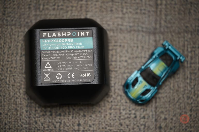 Flashpoint battery pack labeled FPPPX400PRB next to a small blue toy sports car on a textured surface.