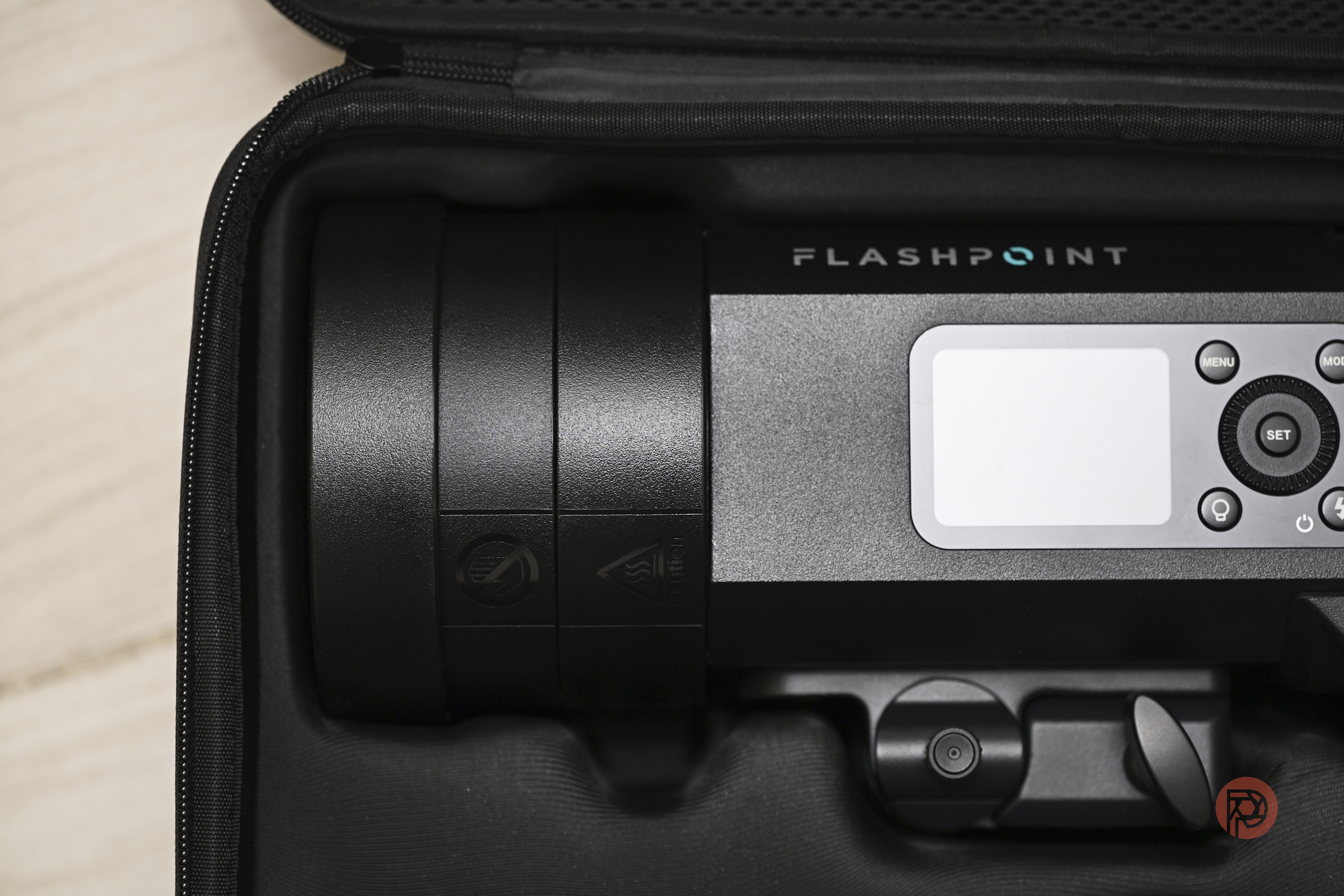 A Flashpoint camera flash unit in a black carrying case, partially shown with control buttons visible.