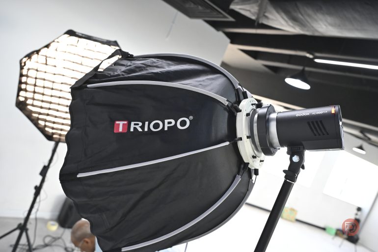Close-up of a Triopo softbox light setup in a bright photography studio with another light in the background.