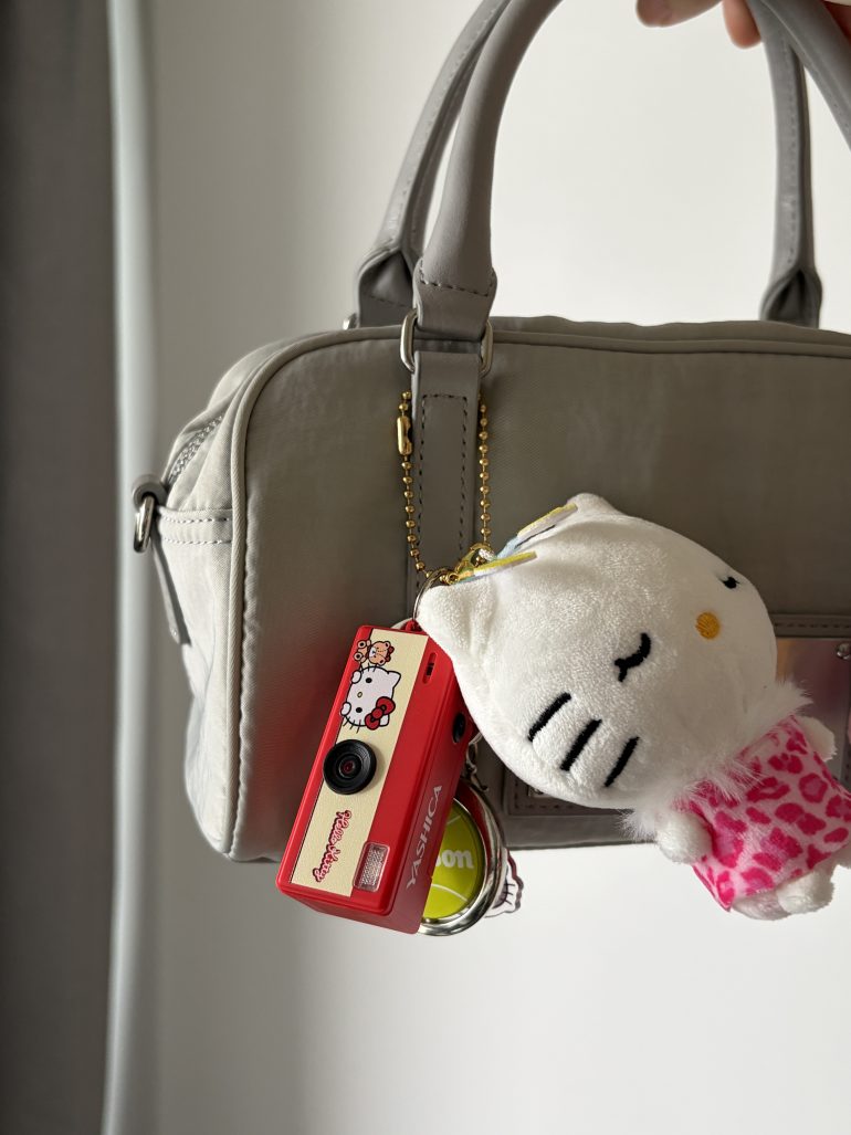 A gray handbag with a Hello Kitty plush and a red camera keychain hanging from the handle.