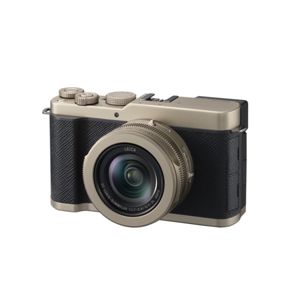 A compact digital camera with a wide lens, black grip, and metallic gold accents, viewed from the front left side.