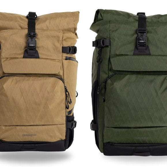 Two roll-top backpacks, one tan and one green, with front pockets and black buckles, standing side by side.