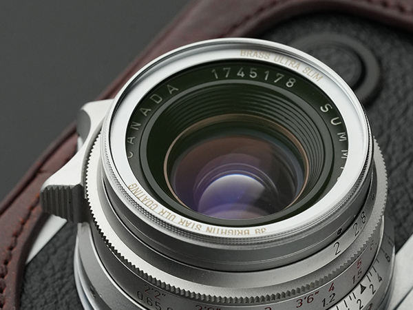 Close-up of a camera lens with visible reflections, mounted on a textured camera body.