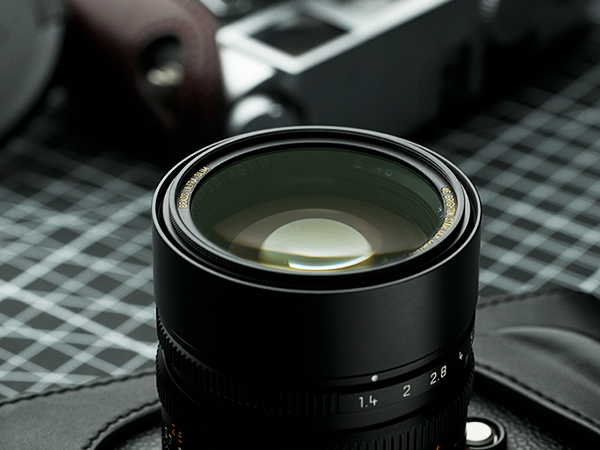Close-up of a camera lens with a blurred camera and grid-patterned background.