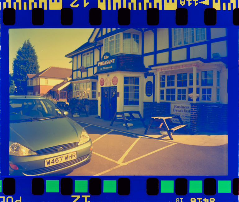A green car is parked outside The Pheasant Inn, with picnic tables and a Business Breakfast sign visible.