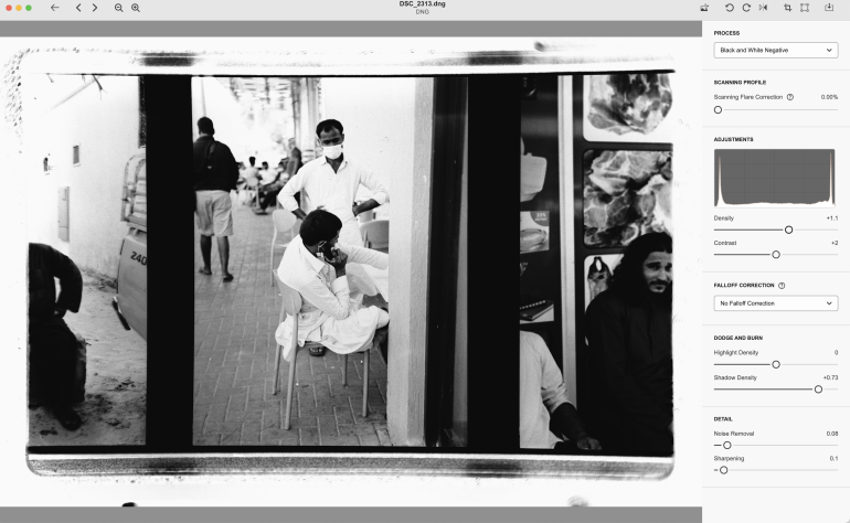 Black-and-white photo of a man getting a shave outdoors, with others walking and sitting nearby.