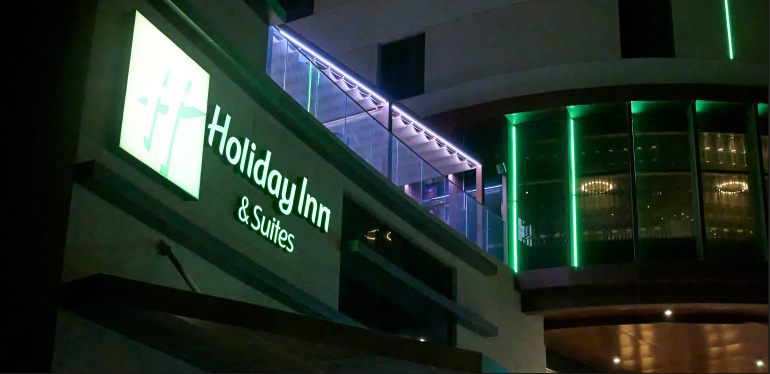 Night view of a Holiday Inn & Suites hotel entrance with green lights illuminating the building.