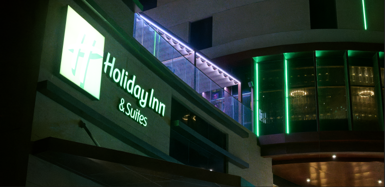 Holiday Inn & Suites sign lit up at night on a modern building with green and purple lights.