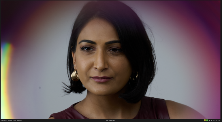 Woman with short dark hair and gold earrings looking ahead, framed by blurred purple edges.