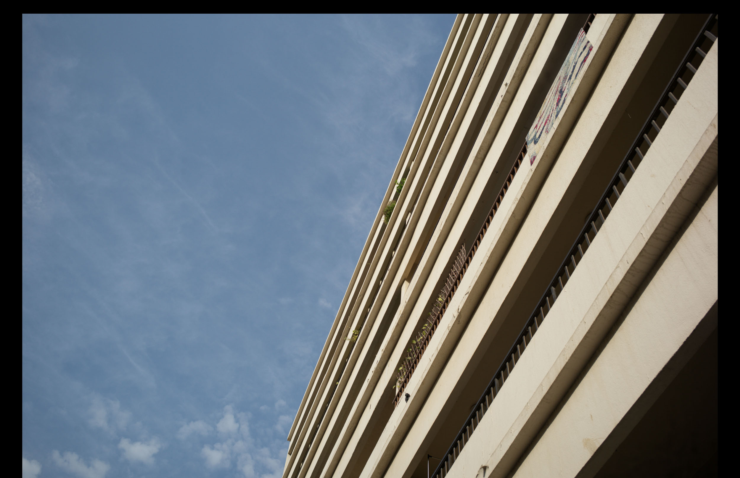 Angled view of a tall beige building with balconies against a blue sky with wispy clouds.