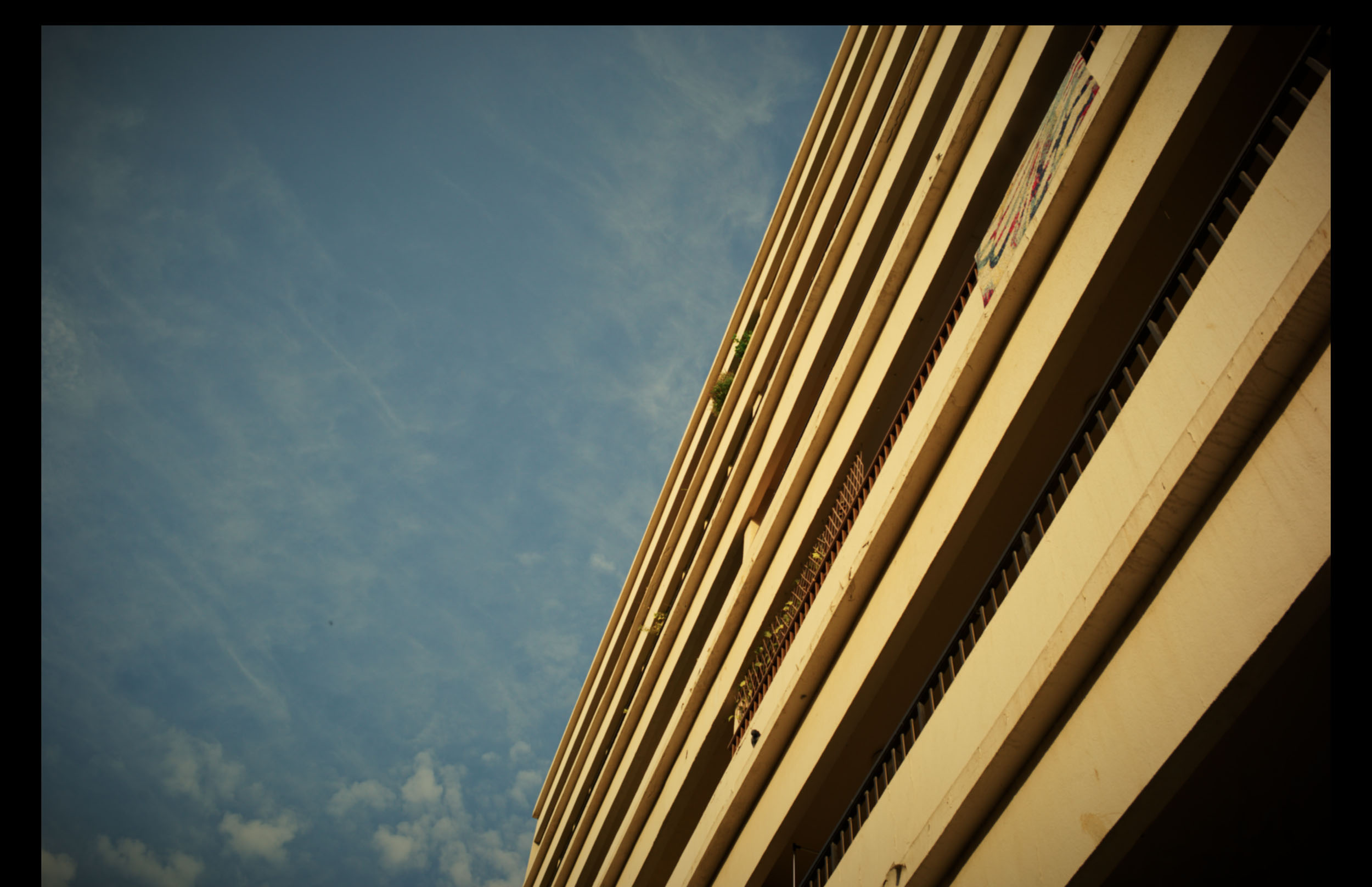 Tall beige building with horizontal lines against a blue sky, viewed from a low angle.