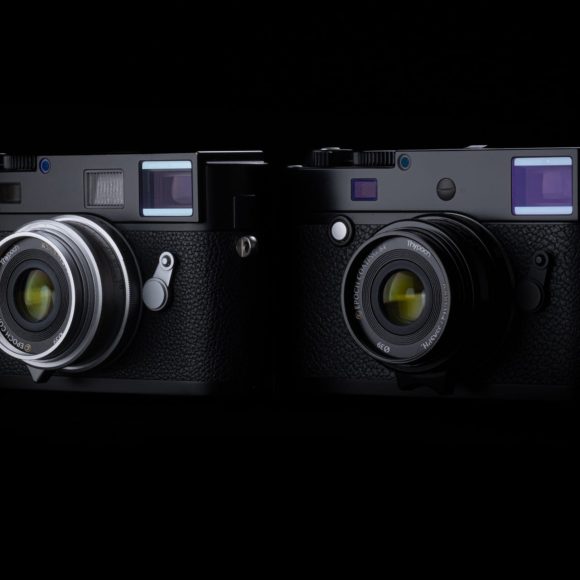 Two black vintage-style cameras with silver and black lenses, side by side against a dark background.