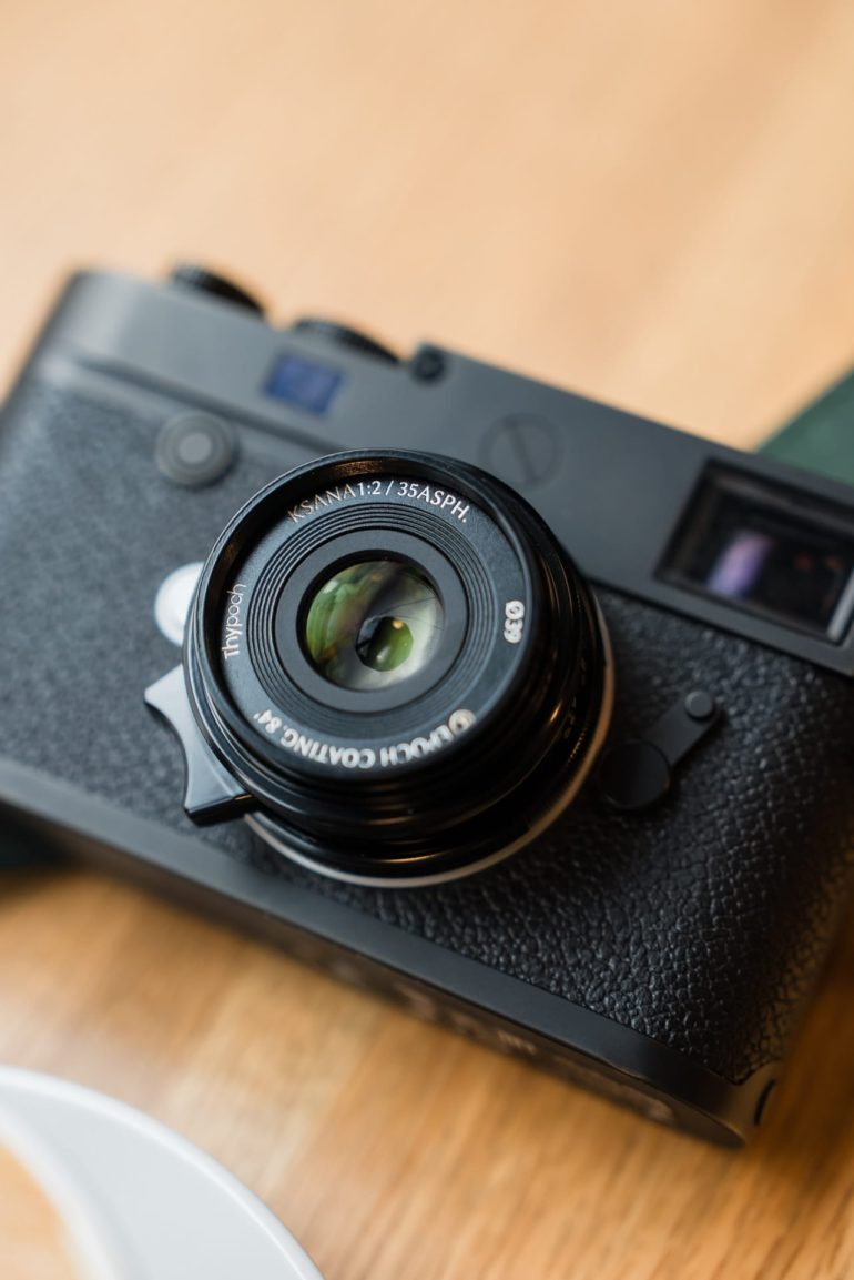 A close-up of a black camera with a 35mm lens resting on a wooden surface.