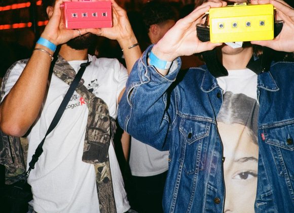 Meet K4MERA: The Most Compelling Digital 3D Camera for Photographers Two people at a party hold up colorful toy cameras, with bright lights and a crowd in the background.