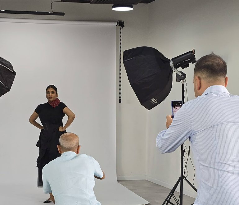 A woman poses in a photo studio while two men take her photo with their phones.