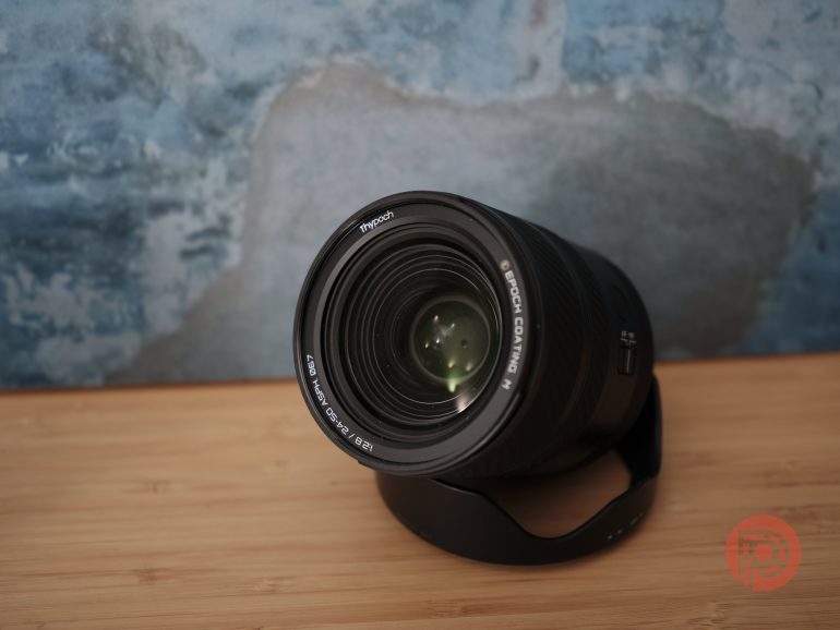 A camera lens on a wooden surface with a blue textured background.