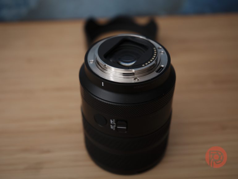 A close-up of a camera lens placed upright on a wooden surface, showing its metal mount.