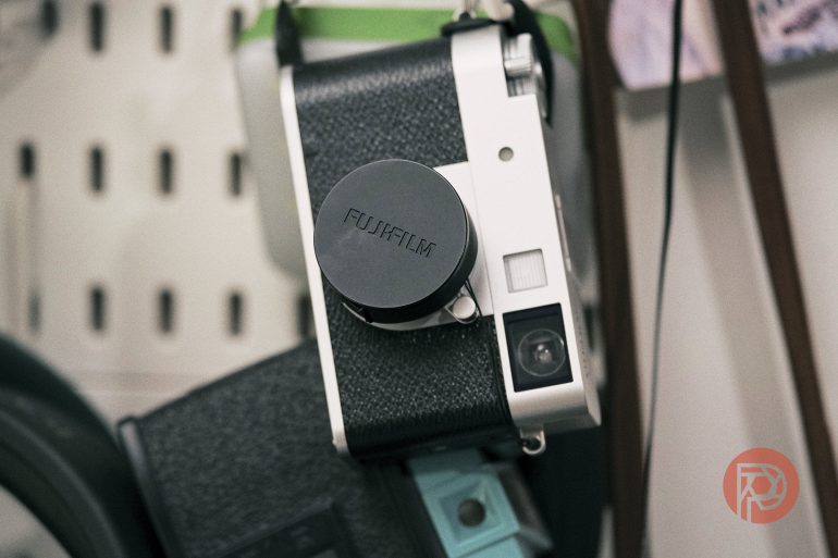 A Fujifilm camera with a lens cap hangs on a wall, surrounded by various objects.