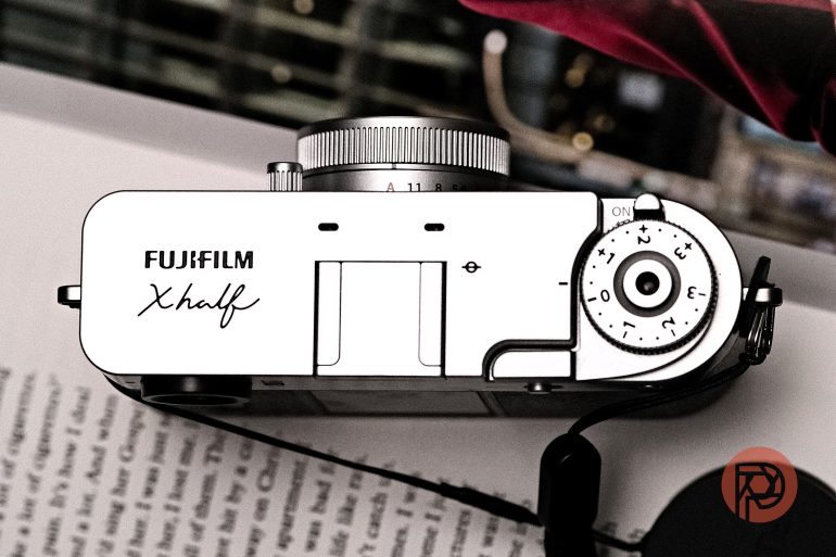 Top view of a Fujifilm X half camera placed on an open book with a blurred background.